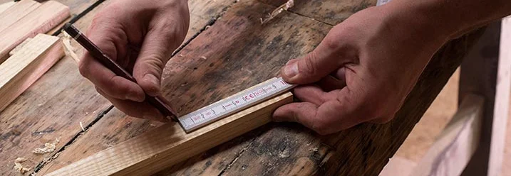 Person misst Holz mit Zollstock und markiert es